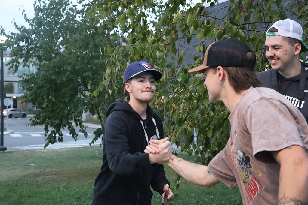 Two friends, Jaden and Nick, dabbing eachother up while another friend watches with a smile.