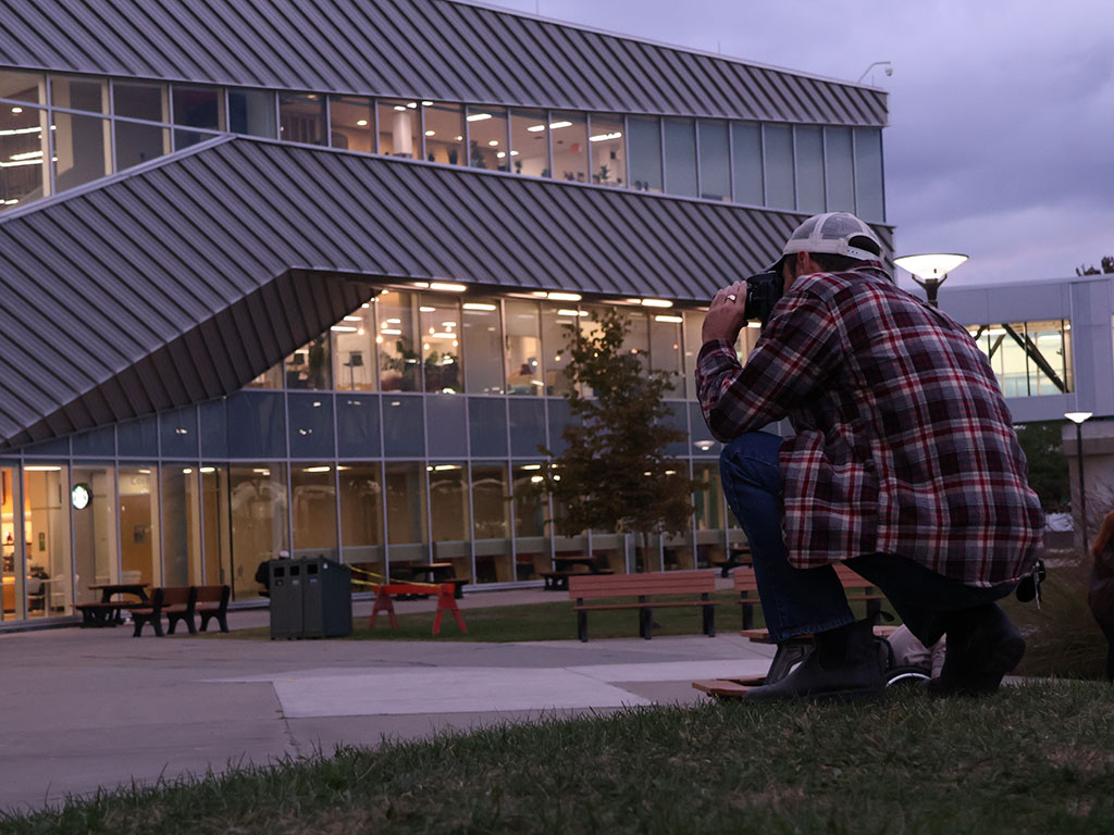 Kevin kneels on the lawn to take a photo outside Student Commons